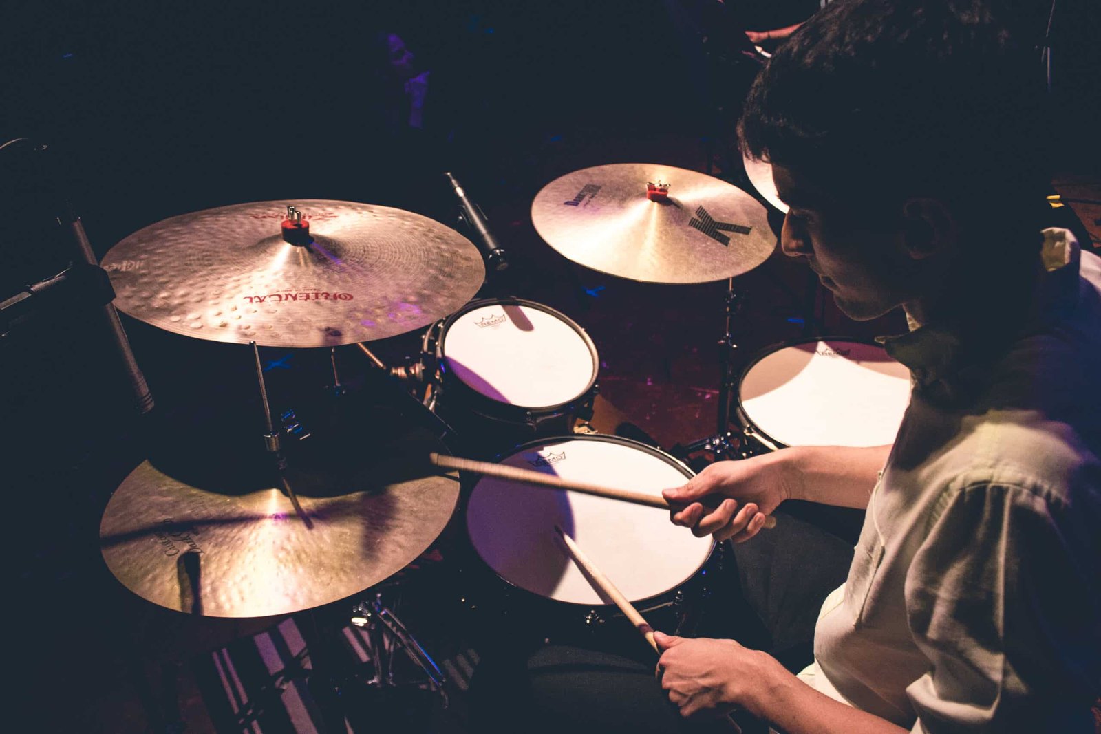 Zeca Vieira tocando bateria em show ao vivo com iluminação de palco, demonstrando a experiência prática aplicada na aula de bateria.