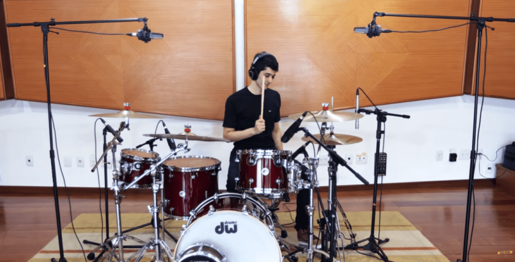 Aluno adulto sorrindo tocando bateria eletrônica em casa durante uma aula de bateria online.