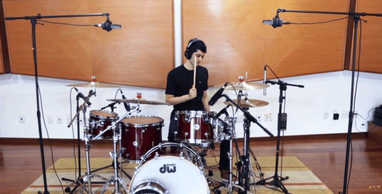 Aluno adulto sorrindo tocando bateria eletrônica em casa durante uma aula de bateria online.