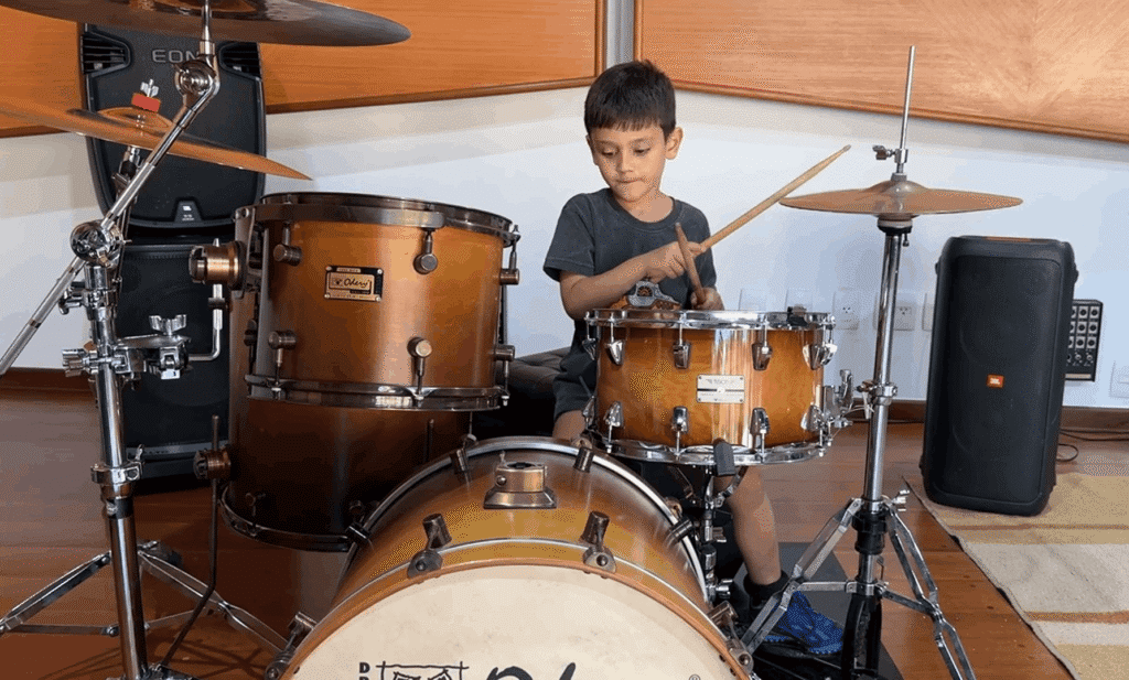 Criança concentrada tocando caixa e bumbo em uma aula de bateria para crianças no estúdio profissional do Zeca Vieira em Valinhos.