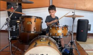 Criança concentrada tocando caixa e bumbo em uma aula de bateria para crianças no estúdio profissional do Zeca Vieira em Valinhos.