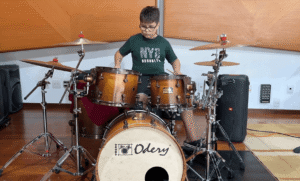 Criança tocando bateria acústica Odery Drums durante uma aula de bateria infantil em Valinhos.
